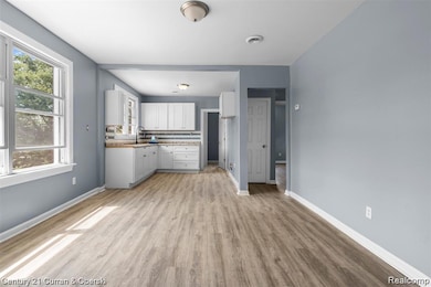 Kitchen with white cabinets, light wood-style flooring, light countertops, and tasteful backsplash