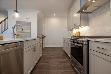 Kitchen featuring appliances with stainless steel finishes, wall chimney exhaust hood, decorative backsplash, dark wood-style flooring, and hanging light fixtures