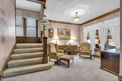 Living area with wallpapered walls, carpet, stairs, a chandelier, and ornamental molding