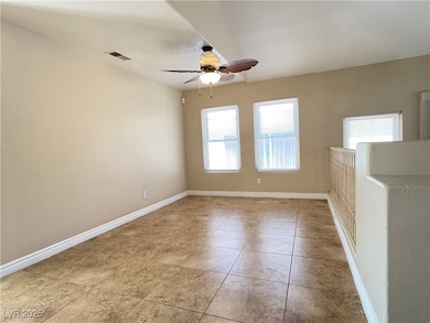 Tiled empty room featuring a ceiling fan and baseb