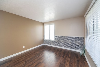 Unfurnished room featuring a textured ceiling, dark wood-style flooring, and wainscoting