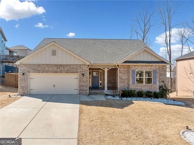 View of front of house featuring brick siding, roof with shingles, fence, a garage, and driveway
