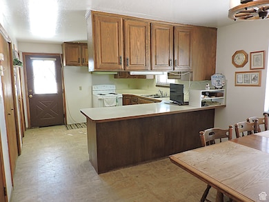 Kitchen featuring a peninsula, light countertops, electric stove, and brown cabinets