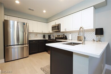 Kitchen featuring appliances with stainless steel finishes, a sink, a peninsula, light stone countertops, and white cabinetry