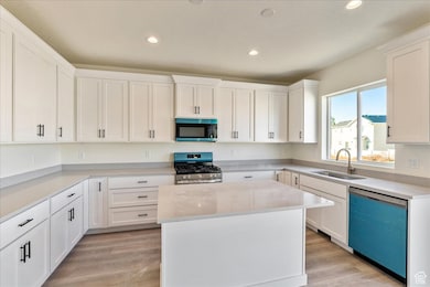 Kitchen with stainless steel appliances, a center island, white cabinetry, light wood-style flooring, and recessed lighting