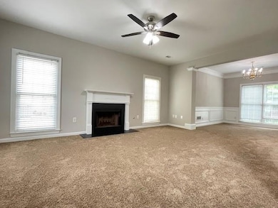 Unfurnished living room with carpet, a fireplace with flush hearth, a chandelier, crown molding, and a ceiling fan