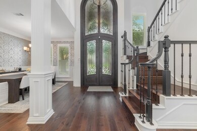 Foyer entrance featuring french doors, decorative columns, dark wood-type flooring, ornamental molding, and a chandelier