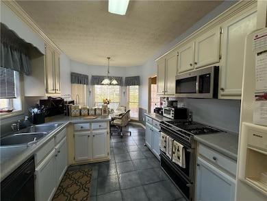 Kitchen featuring a peninsula, black appliances, a textured ceiling, hanging light fixtures, and a chandelier
