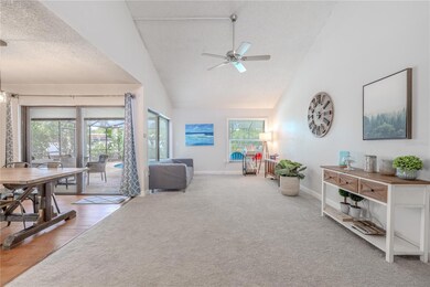 The spacious living room features soaring vaulted ceilings that create an open, airy feel throughout the space. A ceiling fan is centrally mounted to provide comfort and air circulation. The room showcases NEW neutral-toned carpet flooring that flows seamlessly throughout.