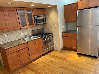 Kitchen with appliances with stainless steel finishes, brown cabinets, glass insert cabinets, dark stone counters, and recessed lighting