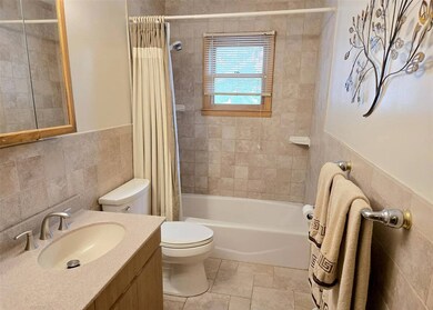 Bathroom with tile walls, vanity, shower / bath combo with shower curtain, wainscoting, and stone tile floors