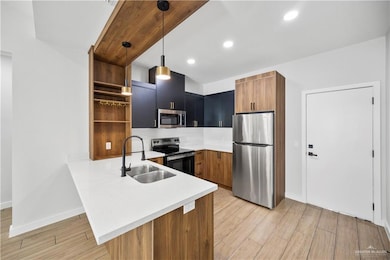 Kitchen featuring stainless steel appliances, a peninsula, a sink, open shelves, and light countertops
