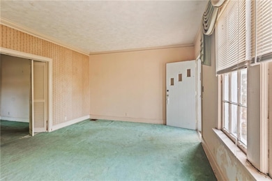 Empty room with carpet flooring, crown molding, baseboards, and wallpapered walls