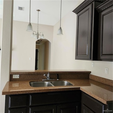 Kitchen featuring a sink, pendant lighting, dark cabinetry, and arched walkways