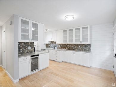 Kitchen featuring white cabinets, tasteful backsplash, light wood-style floors, wine cooler, and glass insert cabinets