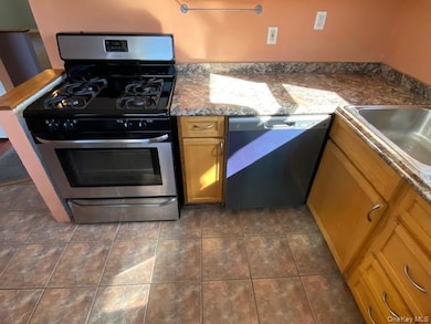 Kitchen with stainless steel gas range, brown cabinetry, black dishwasher, dark stone countertops, and dark tile patterned flooring