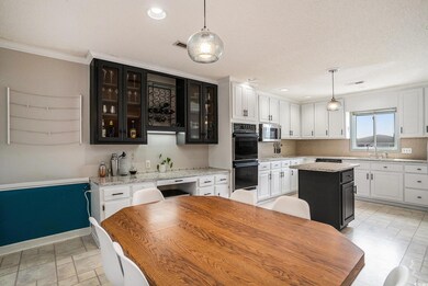 Kitchen featuring white cabinetry, light stone counters, decorative light fixtures, ornamental molding, and recessed lighting