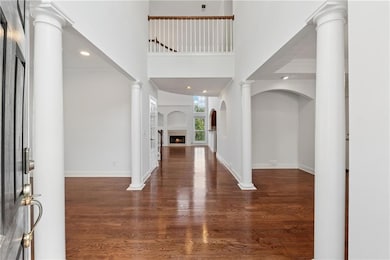 Entrance foyer with decorative columns, dark wood-style floors, a high ceiling, a warm lit fireplace, and recessed lighting