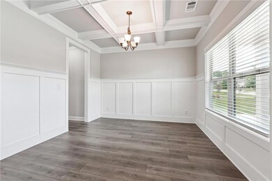 Unfurnished dining area with a decorative wall, a chandelier, coffered ceiling, beam ceiling, and wainscoting