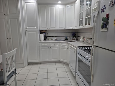 Kitchen with white appliances, white cabinetry, and glass insert cabinets