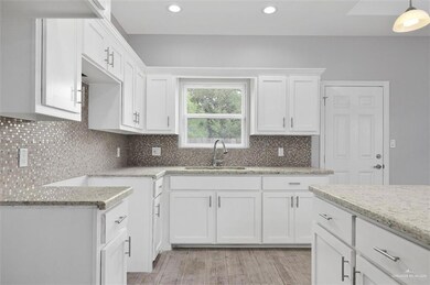 Kitchen with a sink, light stone counters, white cabinets, tasteful backsplash, and recessed lighting