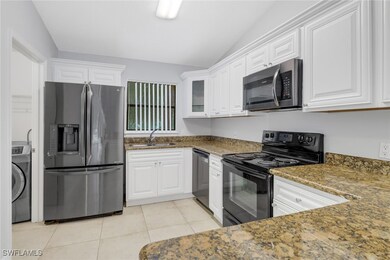 Kitchen featuring stainless steel appliances, lofted ceiling, dark stone counters, white cabinets, and washer / clothes dryer