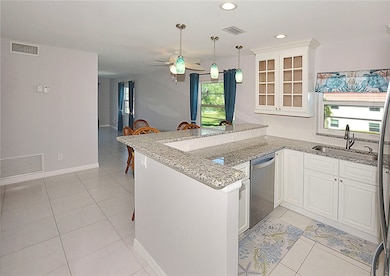 Kitchen featuring glass insert cabinets, a peninsula, light stone counters, recessed lighting, and light tile patterned floors