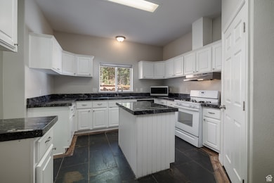 Kitchen with white gas range, white cabinets, and stone tile floors