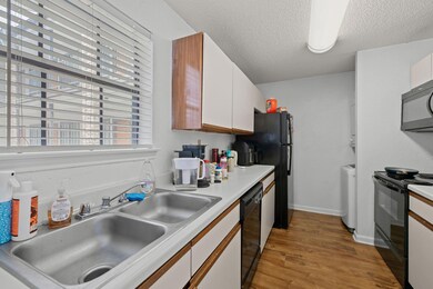 Kitchen with black appliances, light wood-style floors, white cabinetry, a textured ceiling, and light countertops