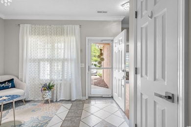 Entryway featuring light tile patterned flooring, crown molding, inlaid floor details, and baseboards