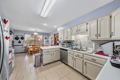 Kitchen featuring backsplash, a peninsula, a textured ceiling, light countertops, and appliances with stainless steel finishes