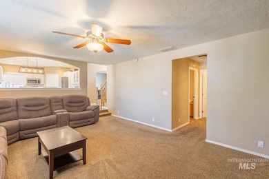 Living room featuring a ceiling fan, arched walkways, a textured ceiling, stairs, and light colored carpet