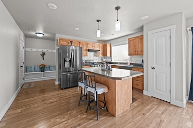 Kitchen with backsplash, hanging light fixtures, stainless steel appliances, a center island, and a breakfast bar area