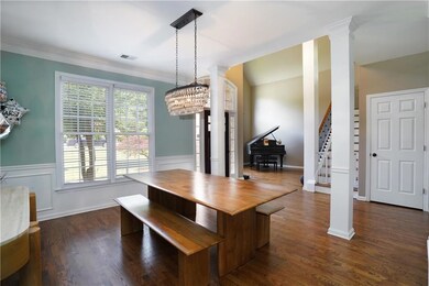 Dining room featuring ornate columns, wainscoting, stairway, dark wood-type flooring, and ornamental molding