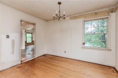 Empty room with crown molding, light wood-style flooring, and a chandelier