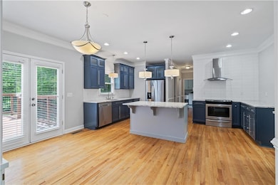 Kitchen featuring wall chimney range hood, stainless steel appliances, blue cabinets, a sink, and ornamental molding