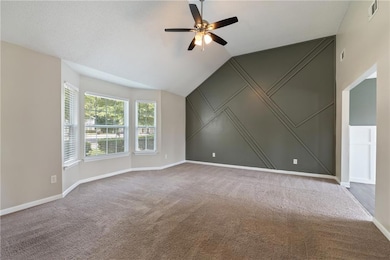 Living room featuring a ceiling fan, carpet floors, and vaulted ceiling