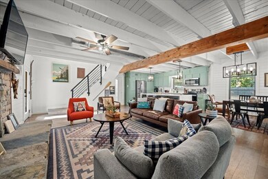 Living room with a chandelier, beam ceiling, light wood finished floors, ceiling fan, and stairs