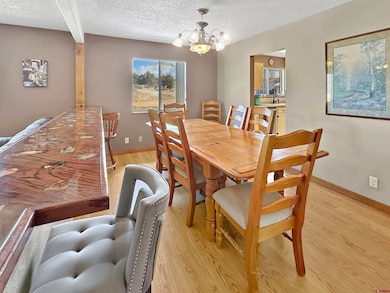 Dining room with baseboards, a textured ceiling, an inviting chandelier, and light wood-style flooring