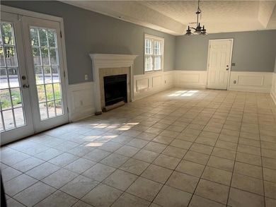 Unfurnished living room featuring a textured ceiling, light tile patterned floors, a decorative wall, a fireplace, and a wainscoted wall