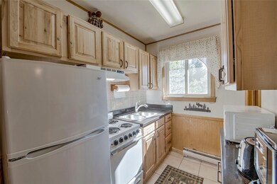 Kitchen with baseboard heating, sink, light tile patterned flooring, light brown cabinetry, and white appliances