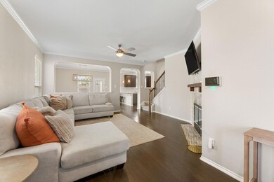 Living area featuring dark wood finished floors, arched walkways, a fireplace with flush hearth, ornamental molding, and stairway