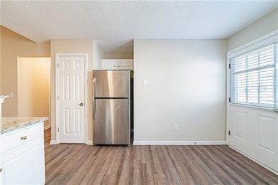 Kitchen featuring light stone countertops, wood finished floors, freestanding refrigerator, and white cabinets
