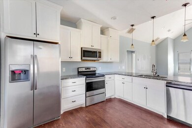 Kitchen with dark wood finished floors, appliances with stainless steel finishes, white cabinets, a sink, and dark stone counters