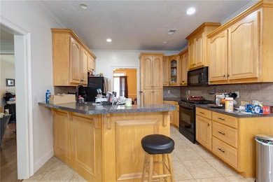 Kitchen featuring black appliances, a peninsula, a breakfast bar area, tasteful backsplash, and light tile patterned floors