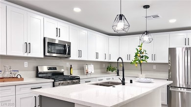 Kitchen with appliances with stainless steel finishes, an island with sink, light stone countertops, white cabinets, and recessed lighting
