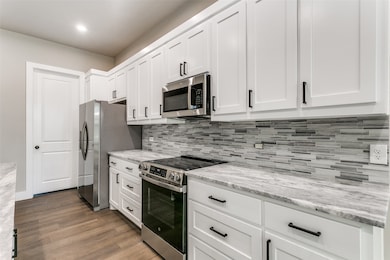Kitchen with appliances with stainless steel finishes, white cabinetry, light stone countertops, dark wood-type flooring, and recessed lighting