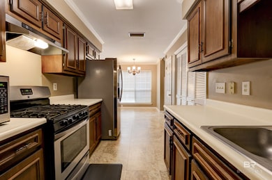 Kitchen featuring crown molding, stainless steel appliances, dark brown cabinetry, a notable chandelier, and light tile flooring