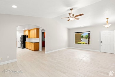 Unfurnished living room featuring light wood finished floors, arched walkways, a ceiling fan, vaulted ceiling, and recessed lighting