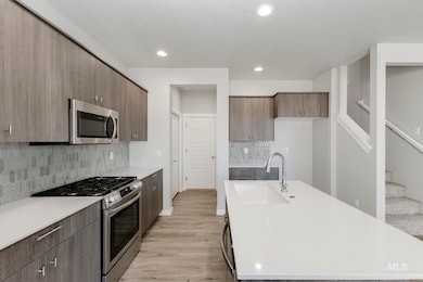 Kitchen featuring appliances with stainless steel finishes, modern cabinets, decorative backsplash, light wood-style floors, and light stone counters